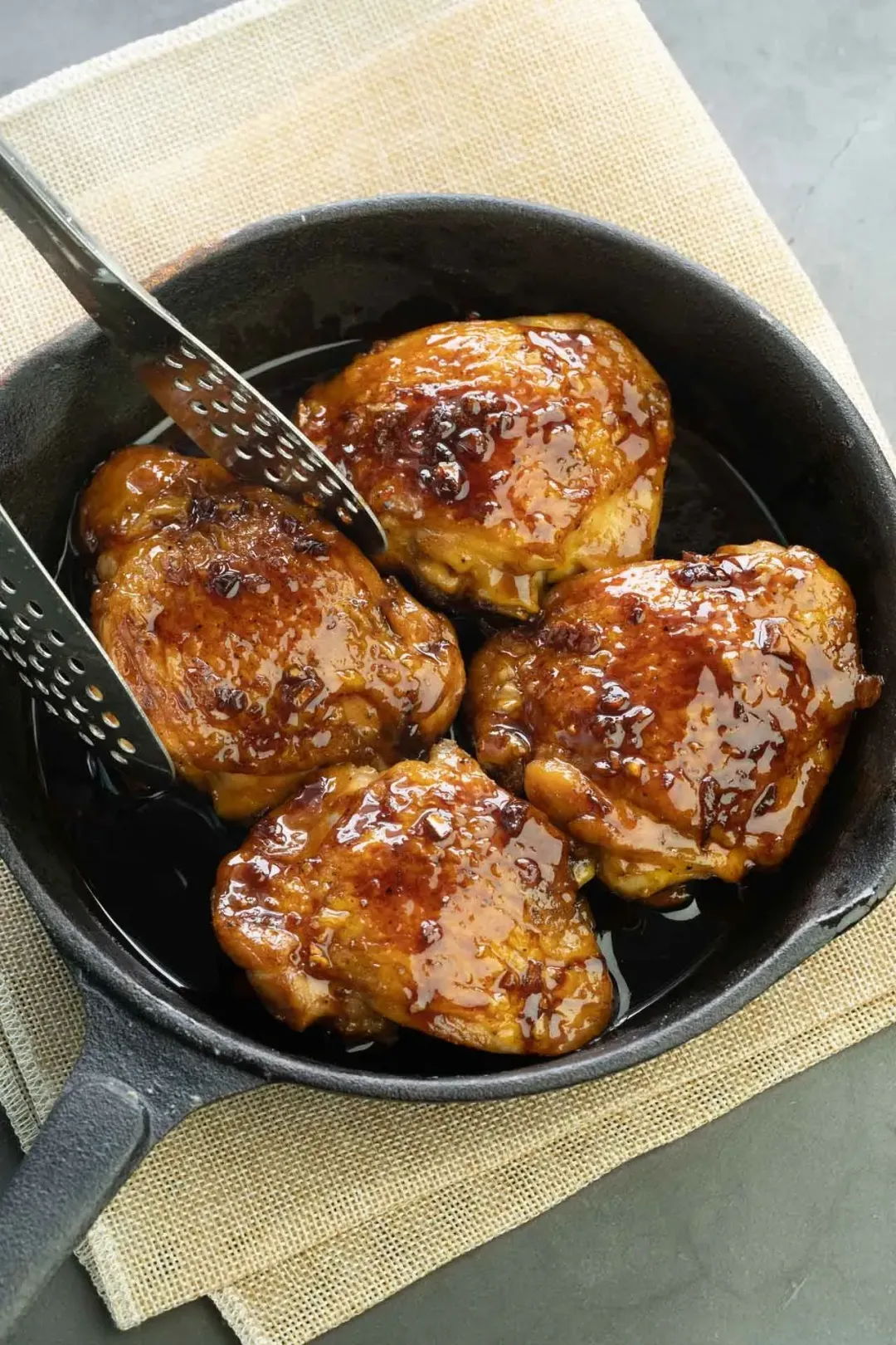 Glossy grilled chicken in a honey-chili glaze in a black skillet on a piece of kitchen cloth