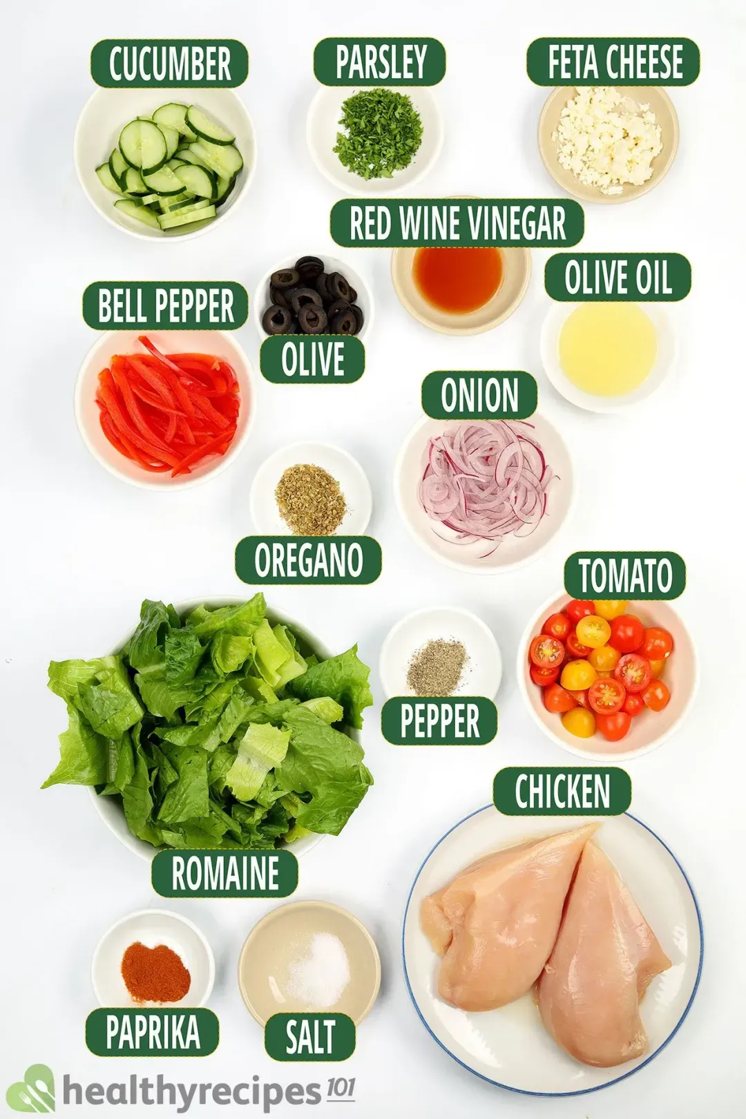 Ingredients for Greek Chicken Salad, including uncooked chicken breasts, leafy greens, cherry tomatoes, and other ingredients.