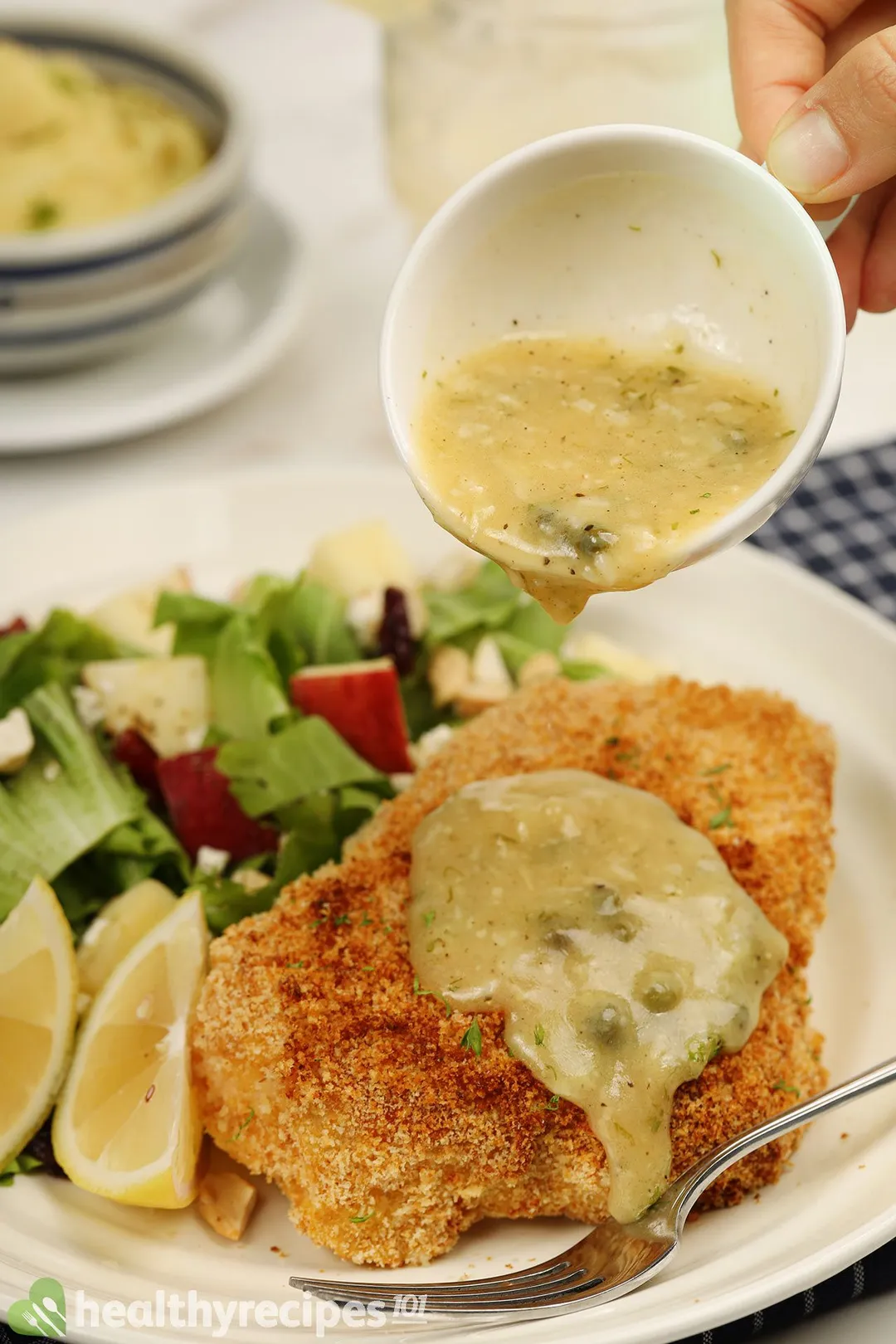 pouring sauce from a cup to a plate of chicken breast and salad