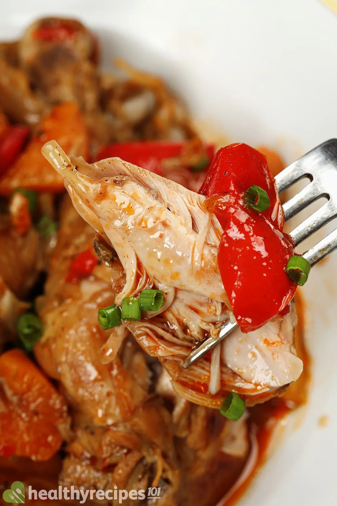 A fork lifting a piece of chicken meat, a piece of bell peppers, and chopped scallions