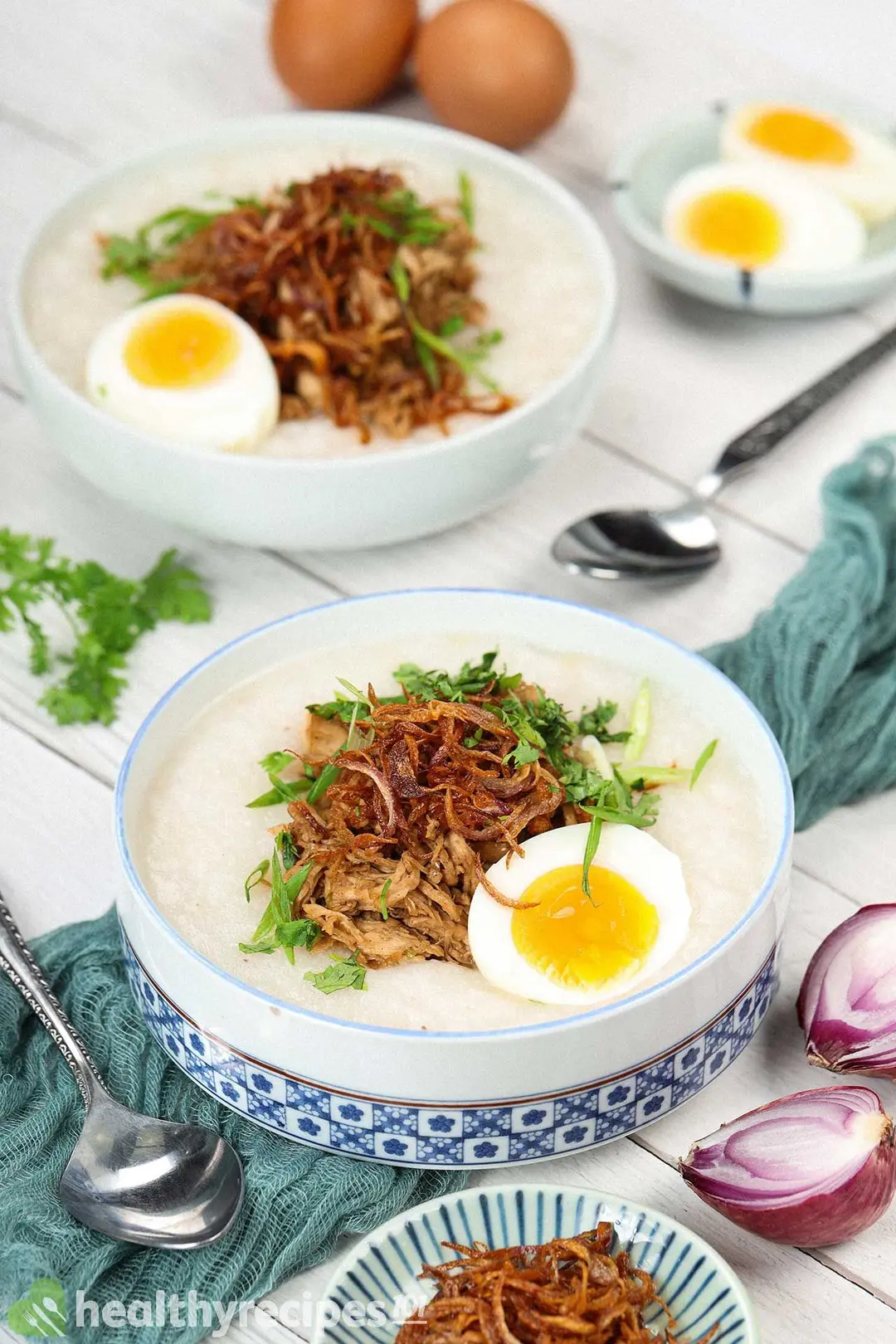 Two bowls of chicken congee with eggs, fried shallots, and herbs