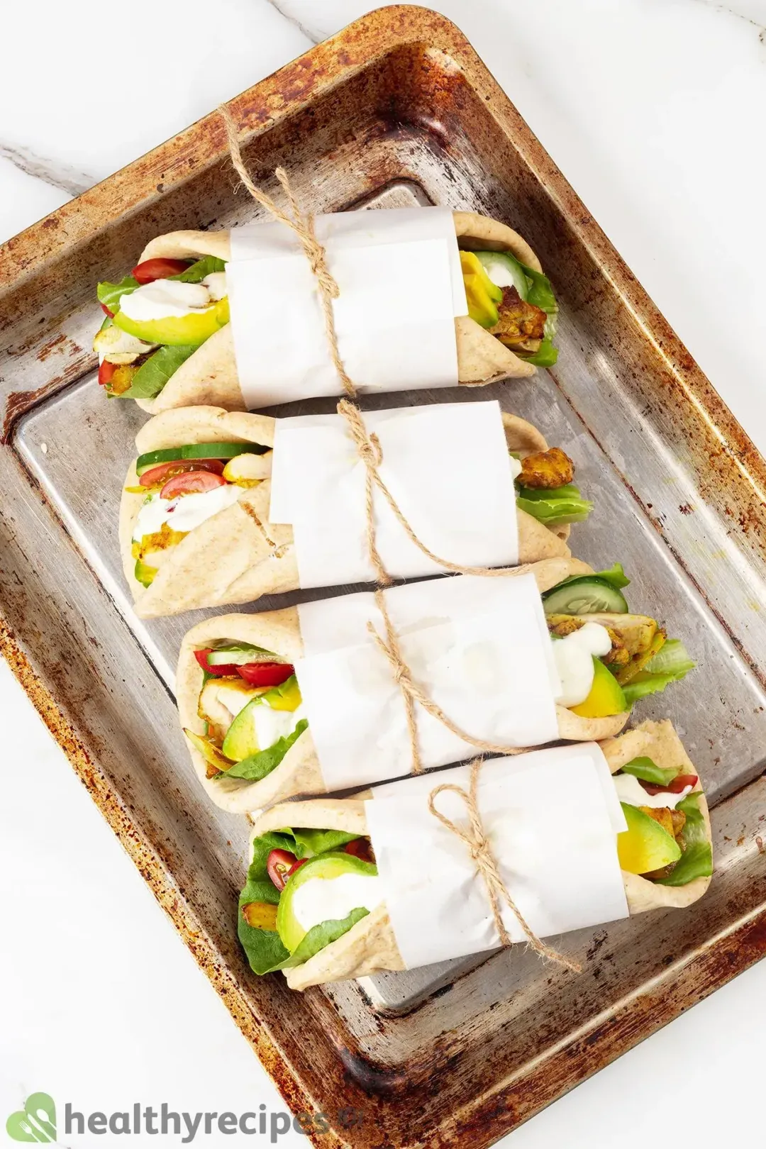 Four chicken shawarma pita wrapped in paper and tied with kitchen twine on a baking sheet