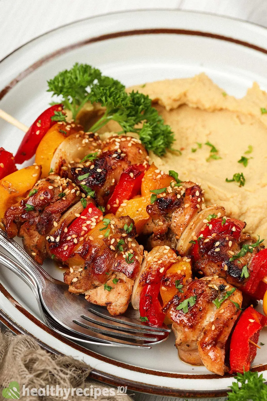 A close-up shot of a plate of chicken skewers served with chickpea puree
