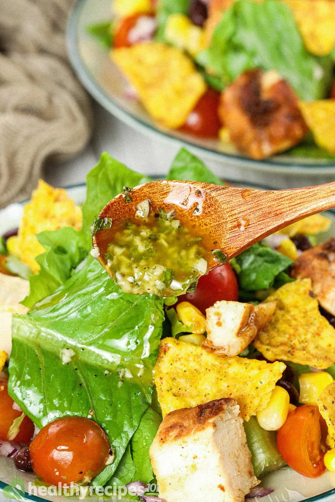 A close-up shot on a wooden spoon slowly pouring dressing onto a chicken taco salad