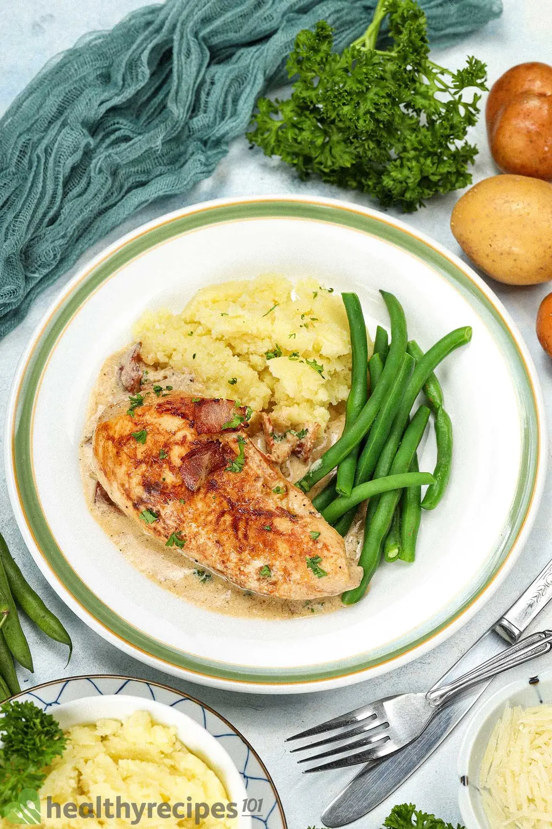 A plate containing a piece of cooked chicken breast, mashed potatoes, and green beans placed next to a fork and a dinner knife