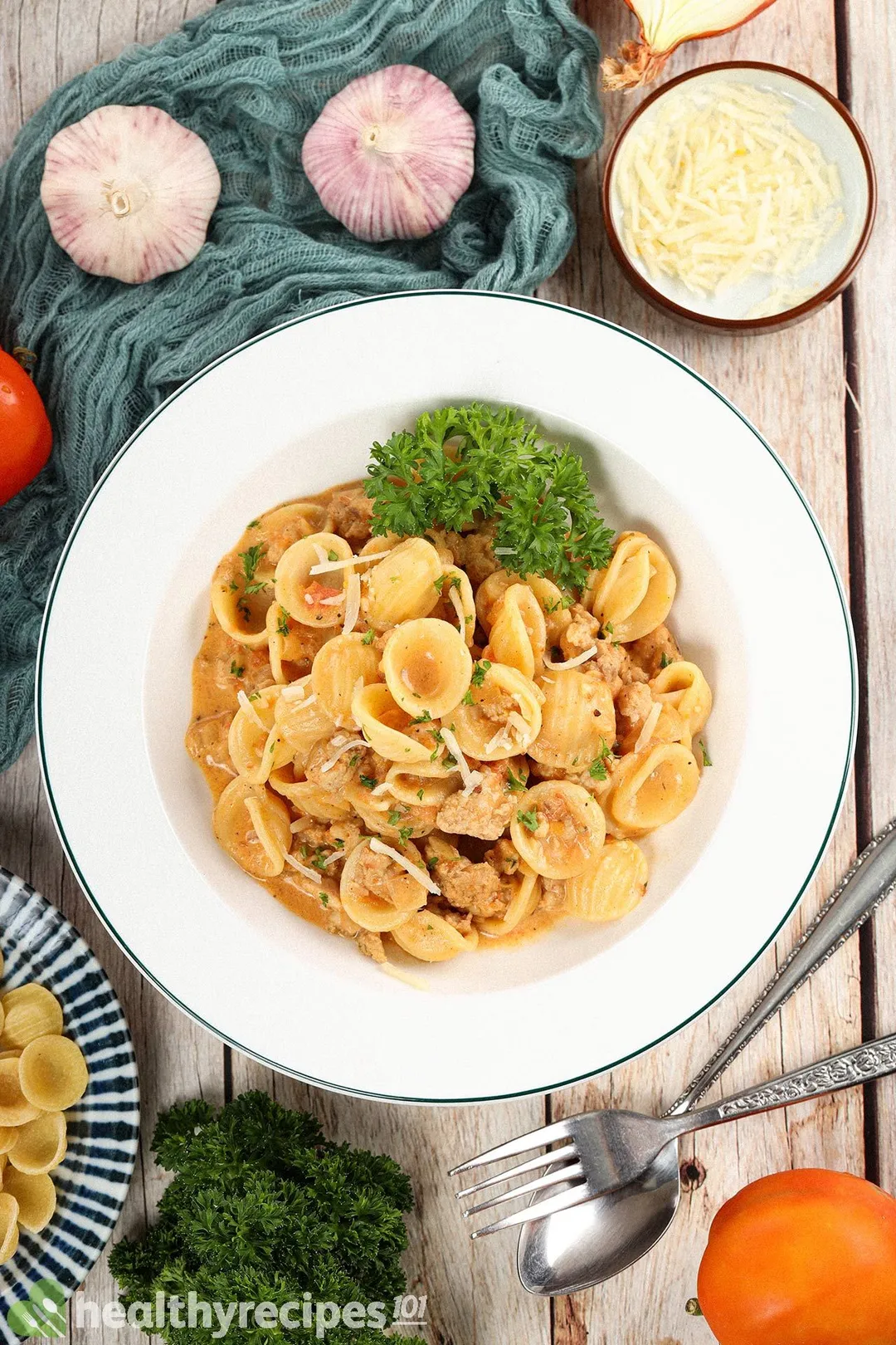 Top-down view of a plate of ground chicken pasta next to a small bowl of shredded cheese