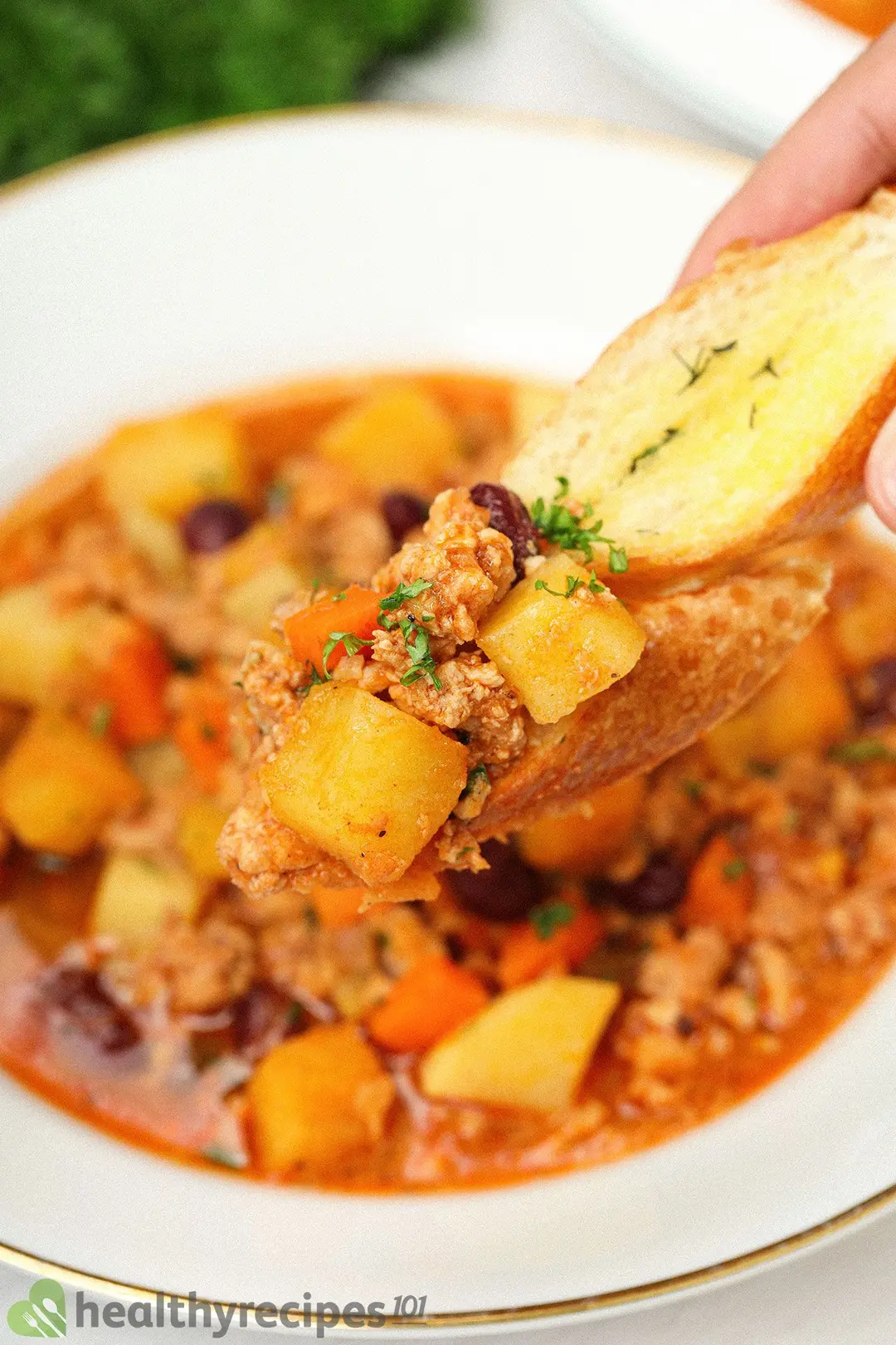 A close-up shot of a diagonally cut slice of baguette with ground chicken, cubed potatoes, and cubed carrots on it