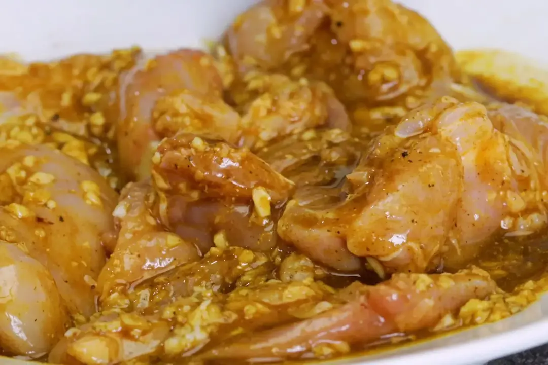 Raw boneless chicken thighs marinated in a marinade full of chopped garlic