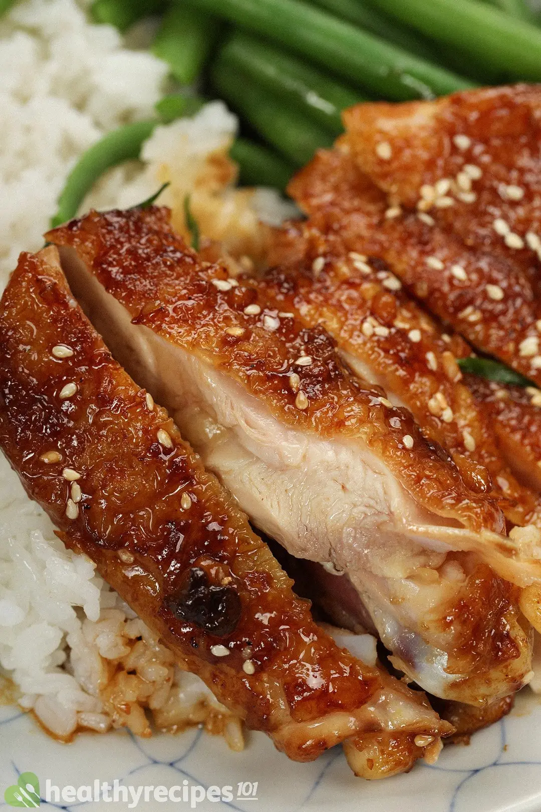 A close-up shot of cooked brown chicken thighs covered in a glossy sauce and white sesame seeds, laid on white rice
