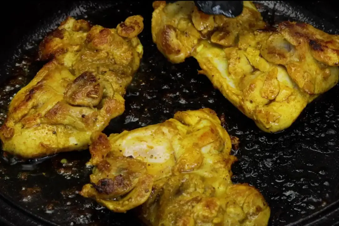 Three pieces of golden deboned chicken thighs sizzling in a cast iron skillet