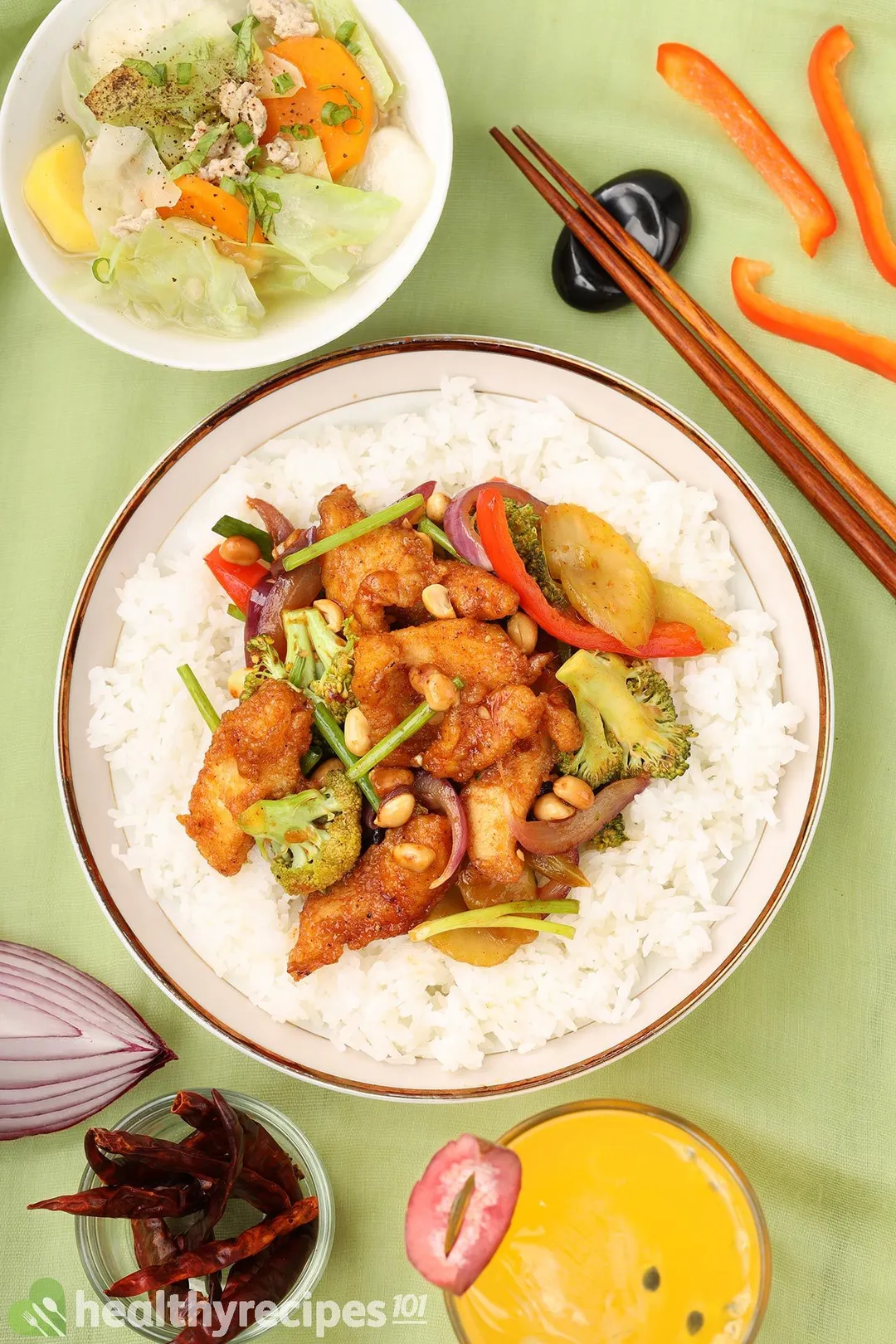 a plat of cooked hunan chicken bed on rice, decorated with a glass of juice and a bowl of soup