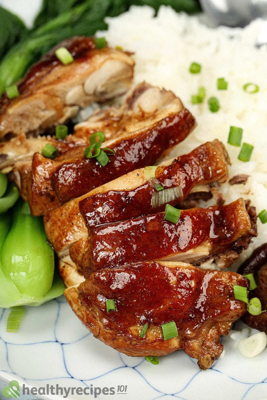 A piece of cooked chicken sliced crosswise into medium pieces, placed next to white rice and bok choy