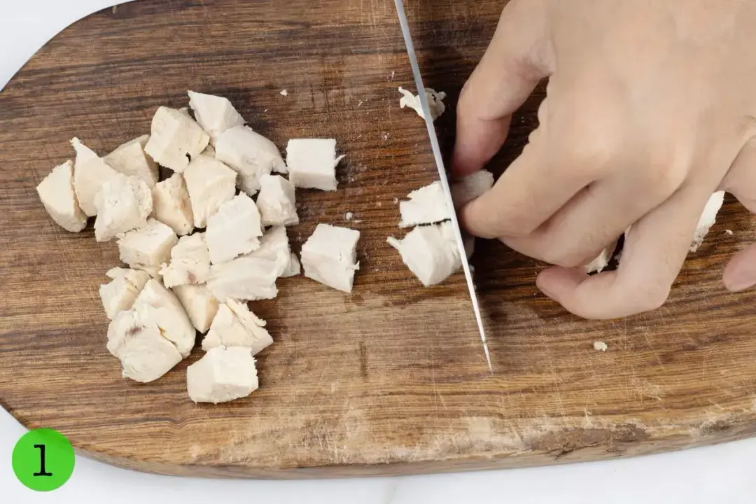 Cooked chicken breasts cut into small cubes on a wooden cutting board