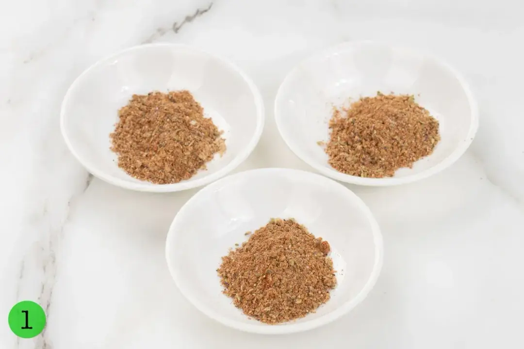 Three equally divided sauce dishes containing paprika, garlic powder, ground black pepper, salt, and dried oregano