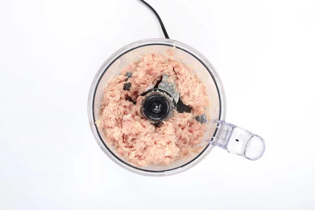 A food processor with raw ground meat inside