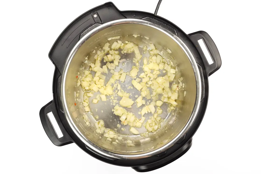 Minced garlic and diced onions being cooked in the inner pot of an instant pot