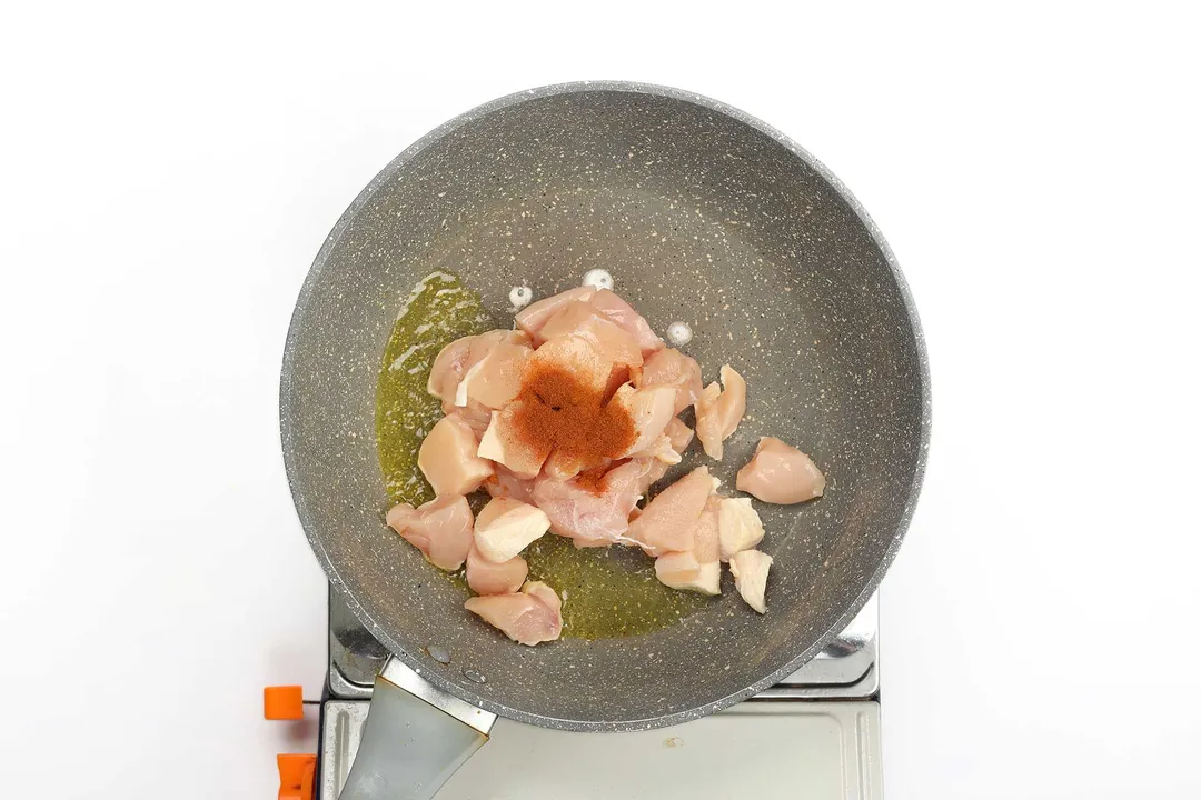 Chicken breast cubes being seared with spices and olive oil in a non-stick skillet