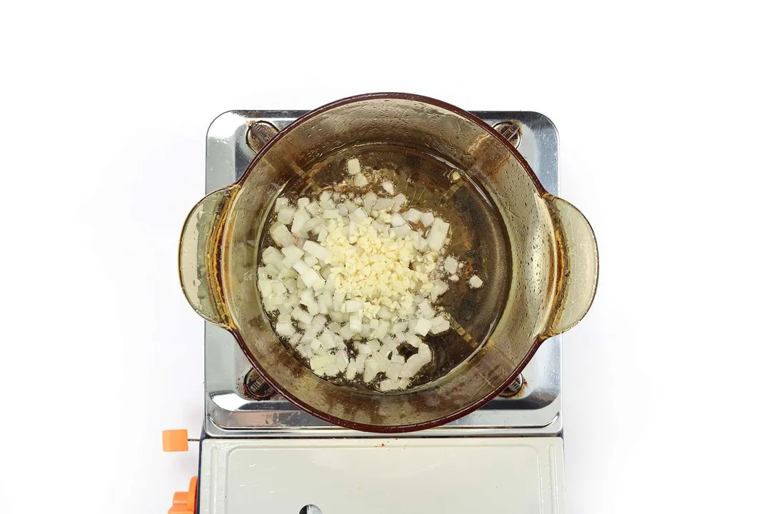 A glass saucepan containing diced onion and diced garlic