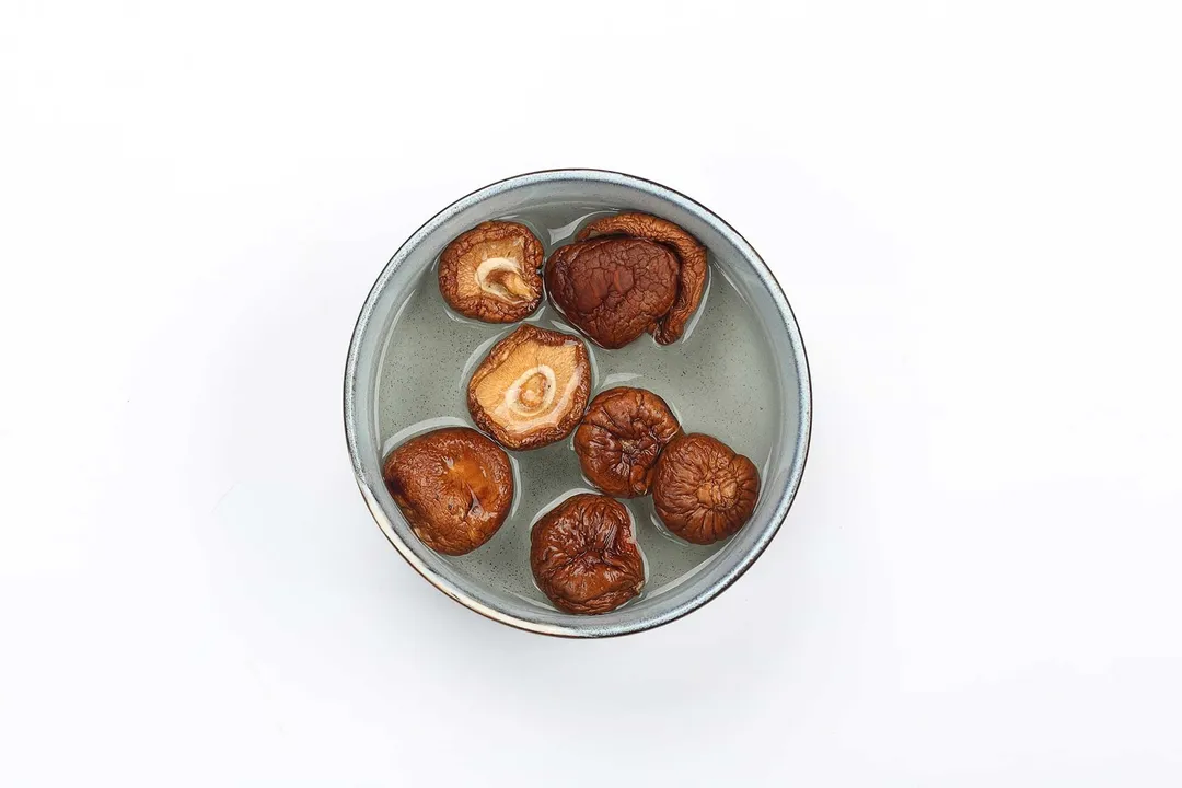 A bowl containing dried shiitake mushrooms being soaked in water