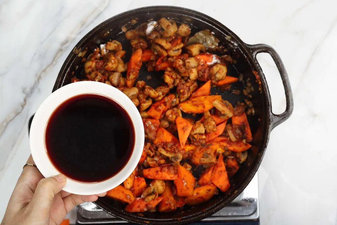 a bowl of red wine on top of cast iron skillet of carrot and mushroom