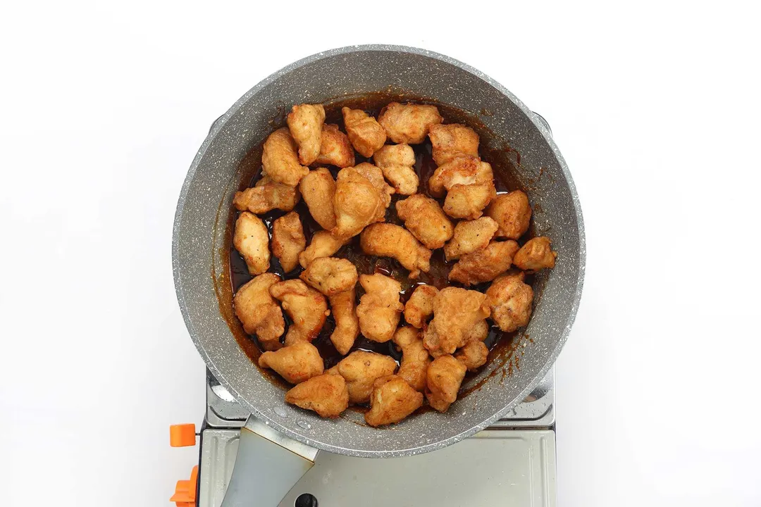 A pan containing various pieces of deep-fried chicken with a dark brown sauce at the bottom