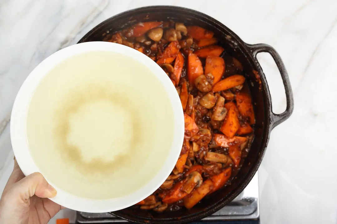 hand holds a bowl of chicken broth on top of a cast iron skillet