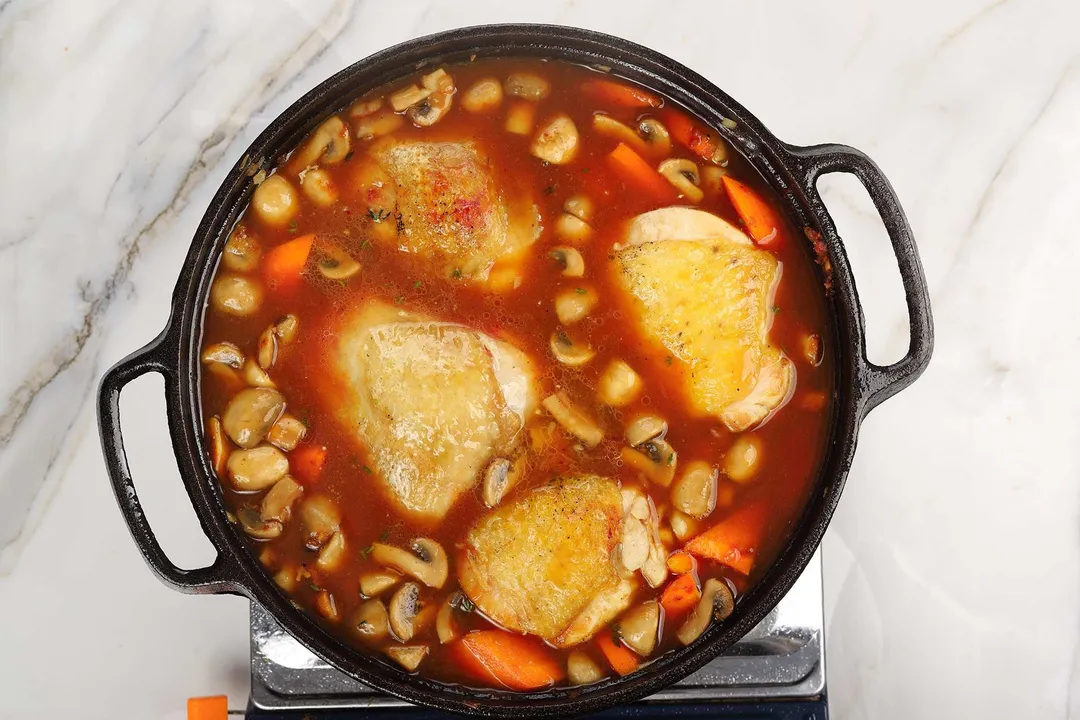 chicken thighs and carrot, mushroom cooking in a cast iron skillet