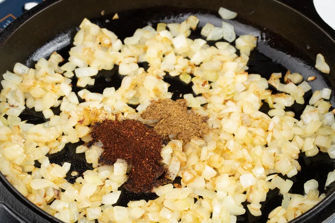 chili, ground cumin and diced onion cooking in a cast iron skillet