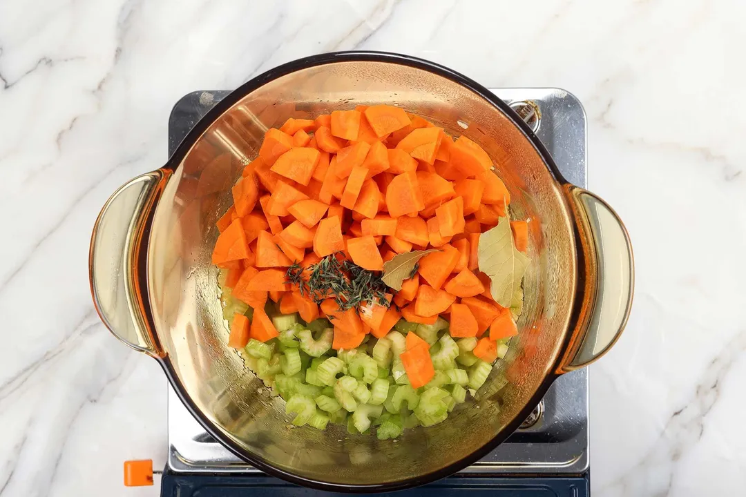 carrot slices, celery slices with thyme and bay leaves in a pot