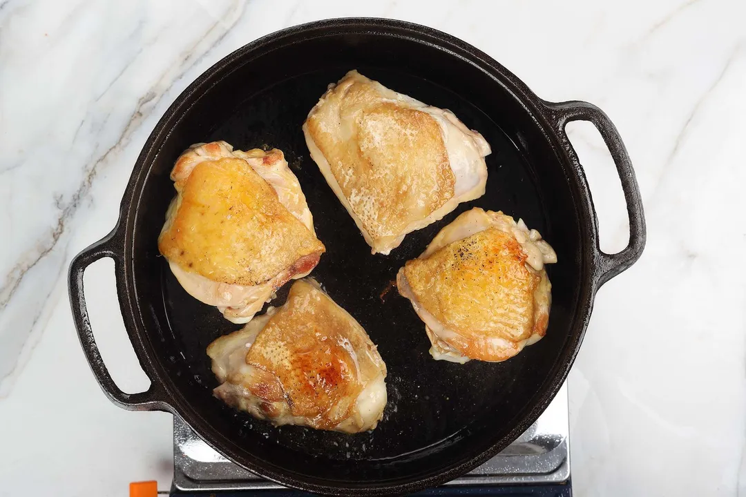 four skin up chicken thighs cooking in a cast iron skillet