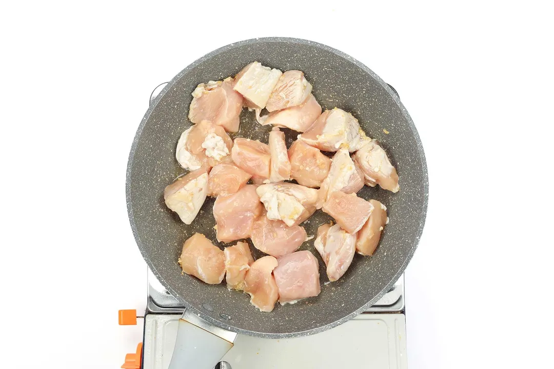 A large pan cooking large cubes of raw chicken