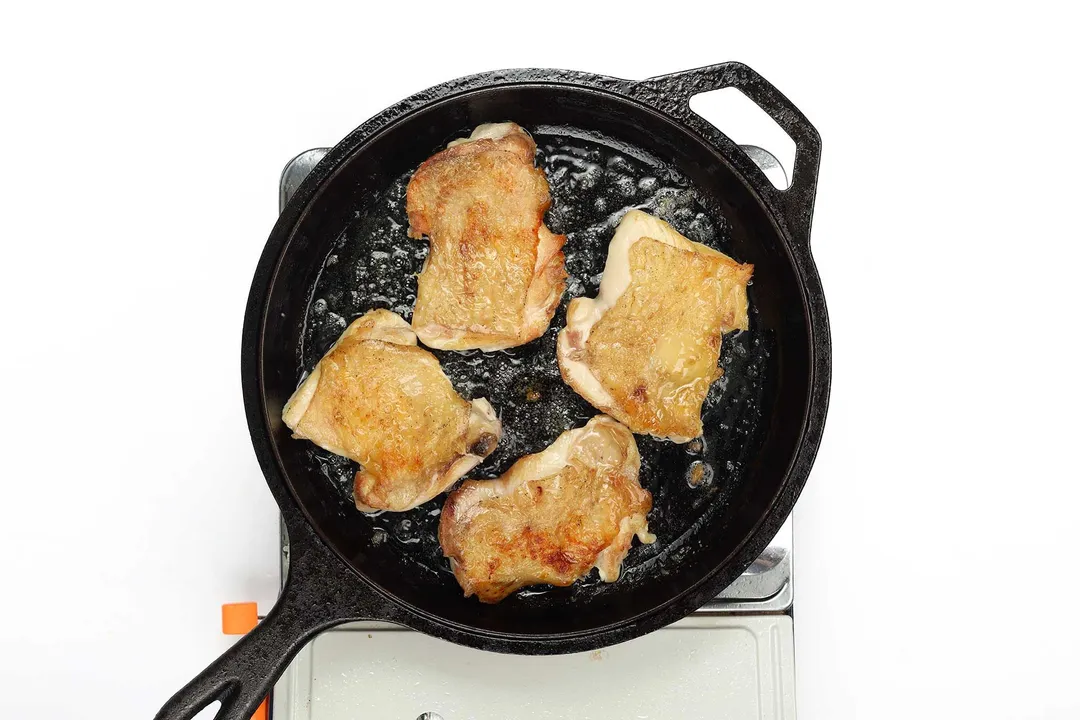 Chicken thighs being seared in a cast iron skillet