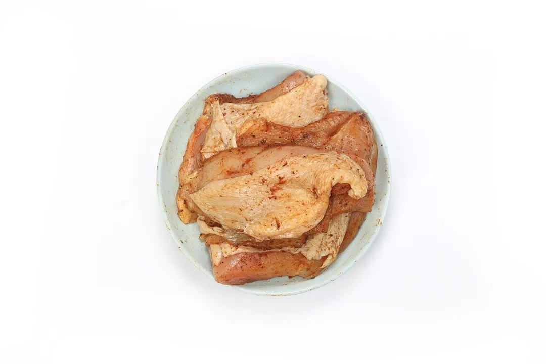 A plate containing four pieces of raw chicken thighs covered in paprika