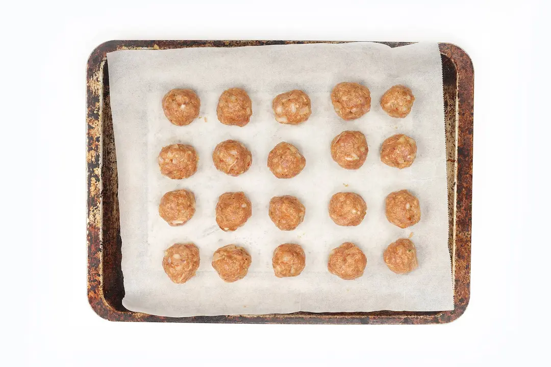 Equal-sized chicken meatballs on a lined baking tray