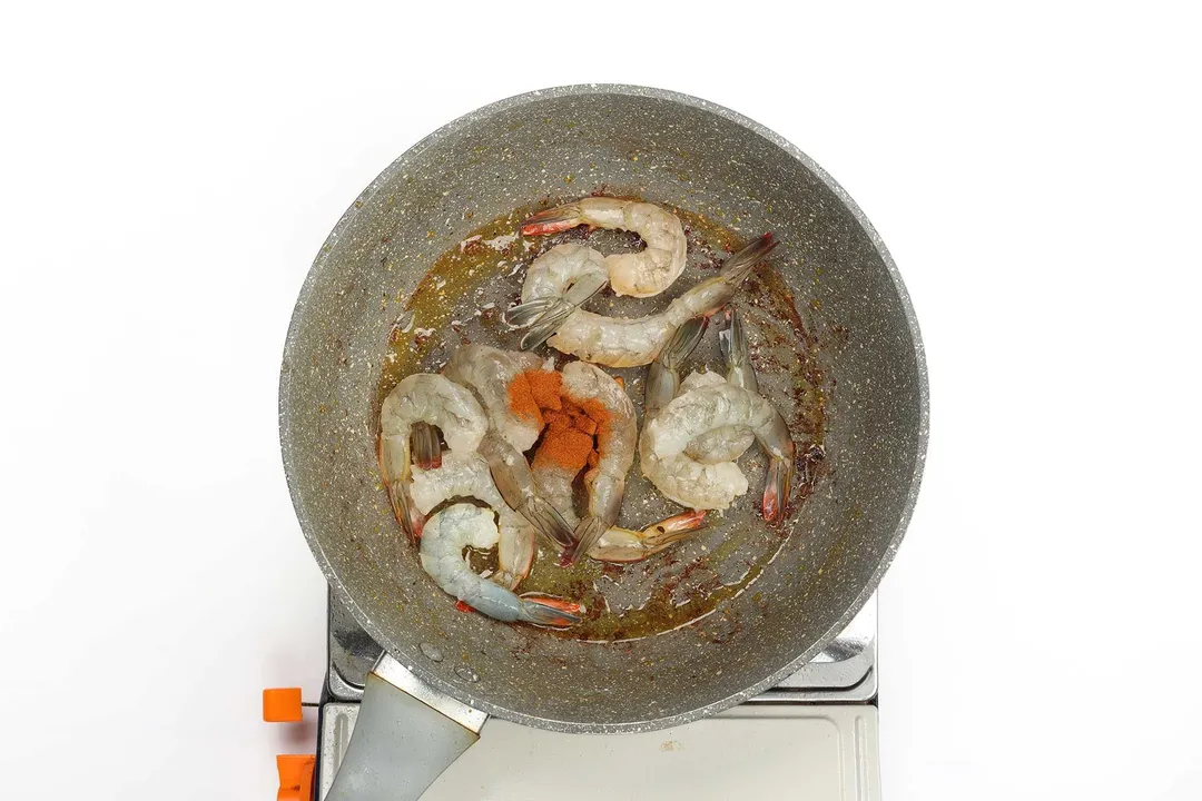 Peeled shrimp being cooked with paprika in a non-stick pan