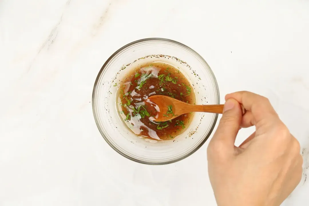 A hand using a wooden spoon to stir a dark brown sauce.