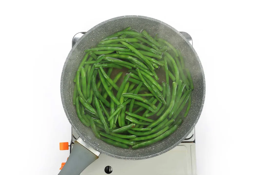A large pan cooking a lot of green beans in boiled water