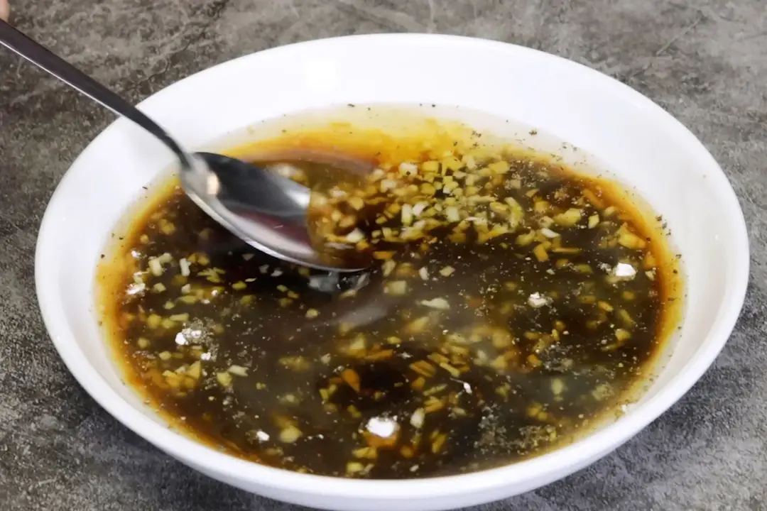 A shallow bowl of sauce, garlic, and oil stirred together with a spoon