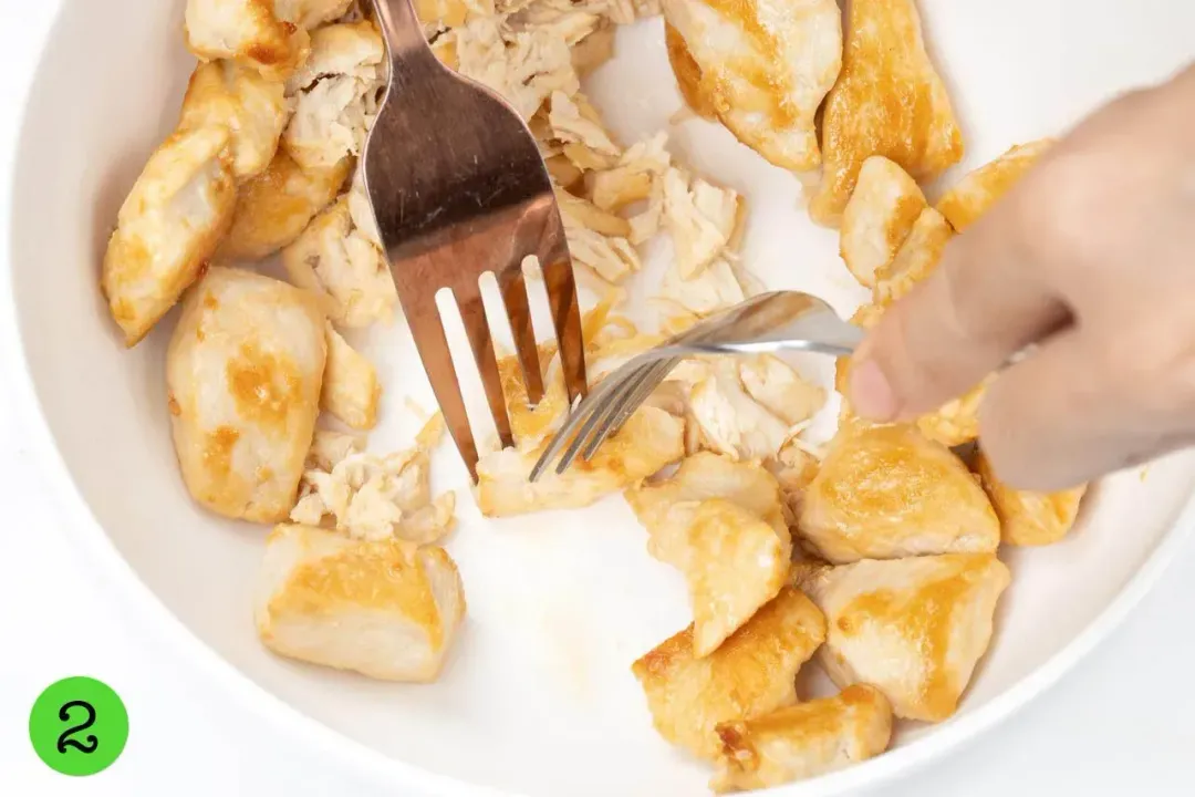 Two hands using forks to Shred cooked chicken