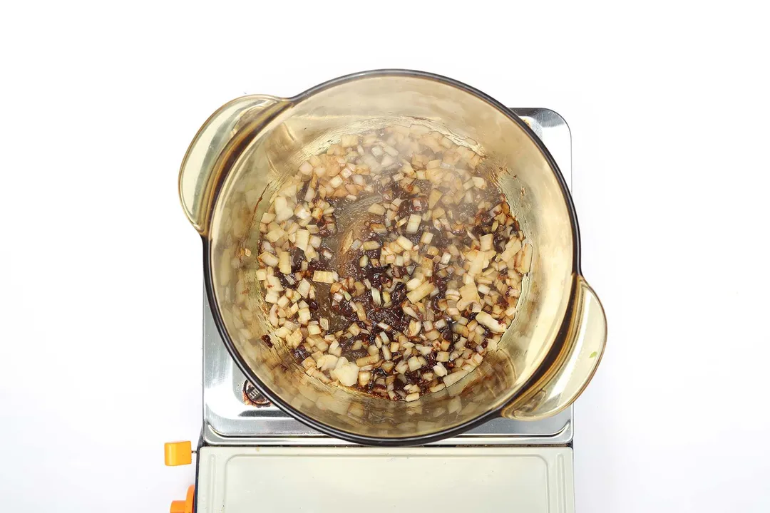 A saucepan cooking a caramelized mixture of aromatic vegetables with smoke steaming up