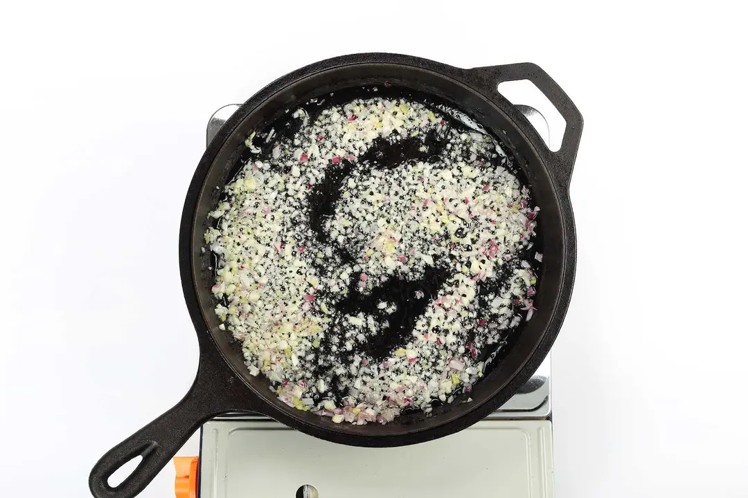 A skillet cooking finely minced red onions and finely minced garlic
