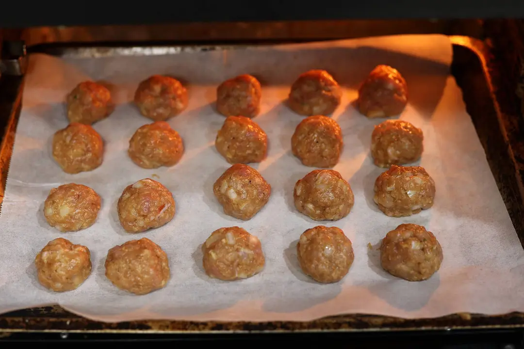 Chicken meatballs on a lined baking tray in the oven