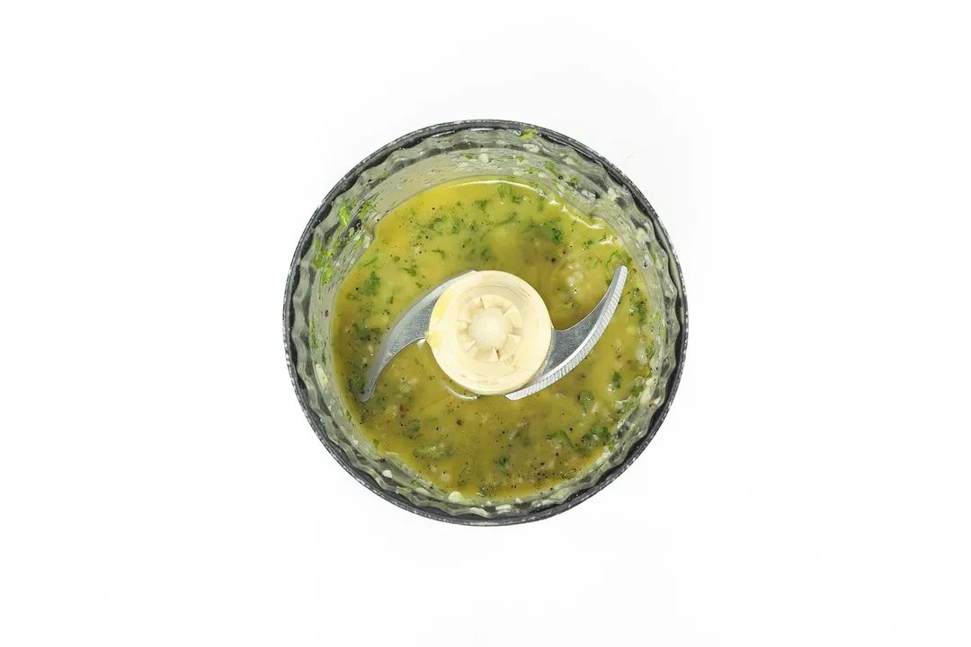 A food processor filled with green salad dressing and herbs