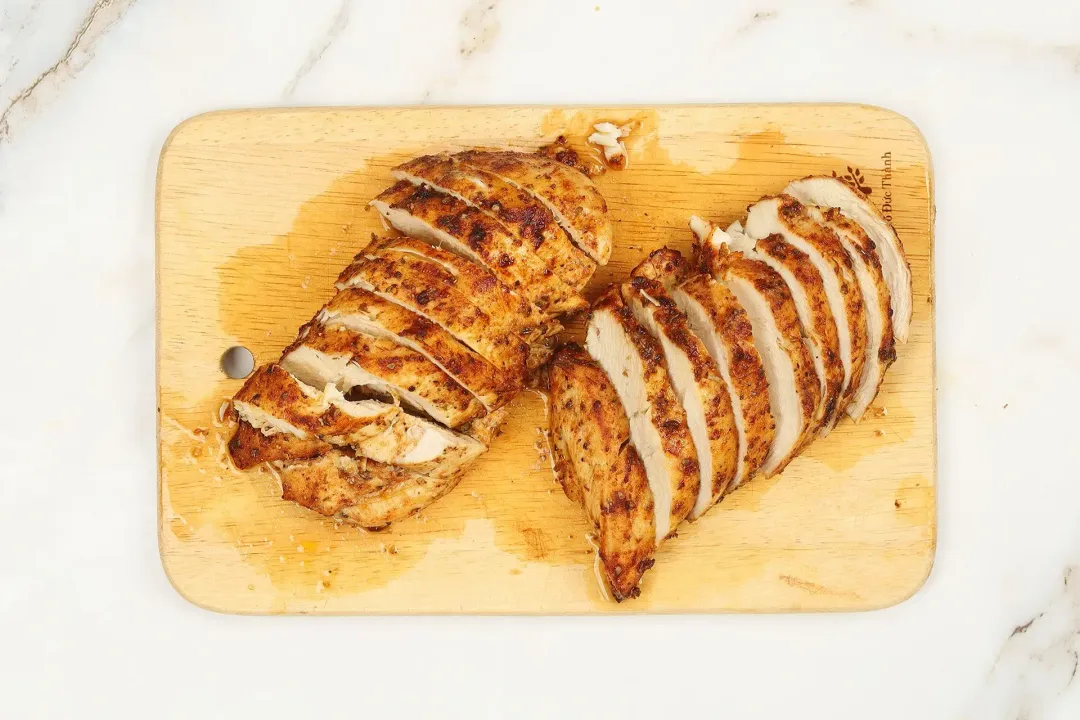 Sliced cooked chicken with brown exterior and white meat on a chopping board