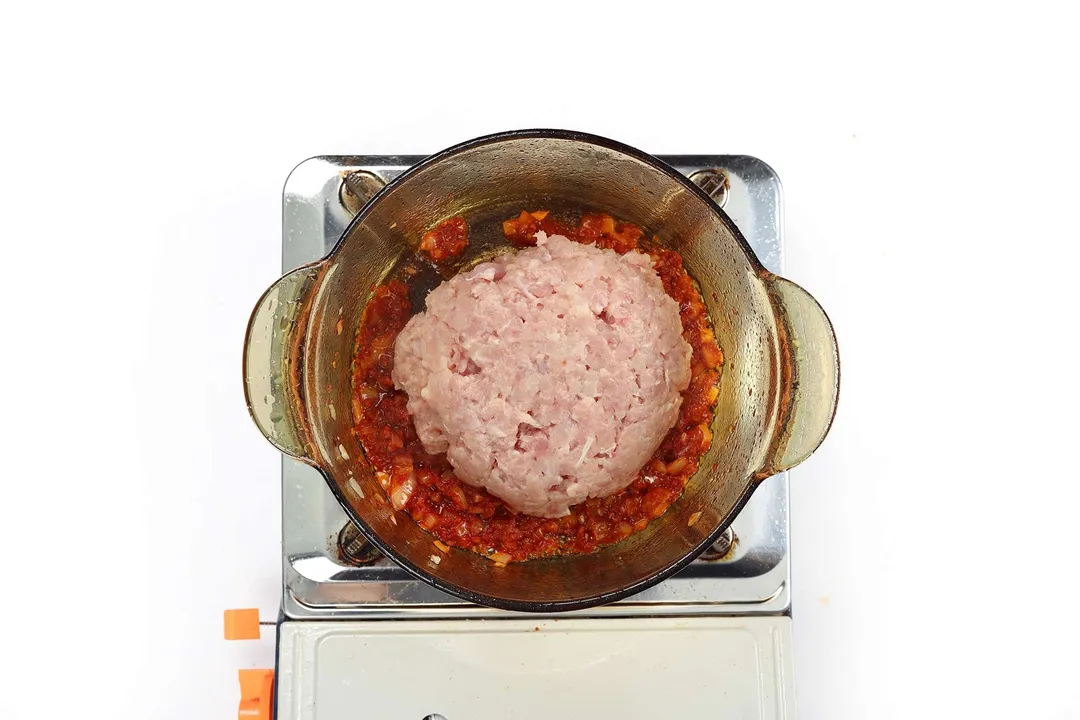 A glass saucepan cooking aromatics and a large lump of ground meat