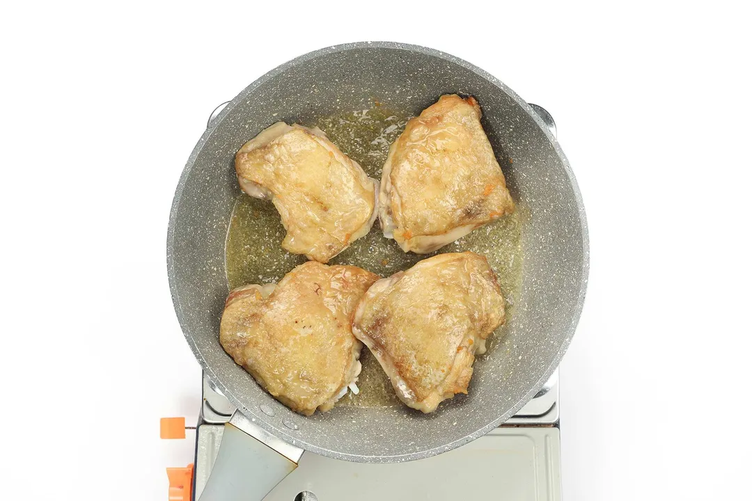 A large pan cooking four pieces of chicken thighs with some oil underneath