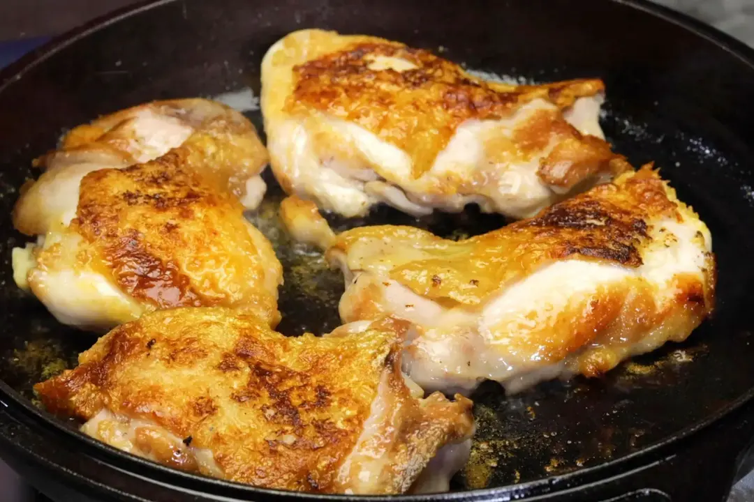 Sizzling golden brown chicken thighs in a cast iron skillet