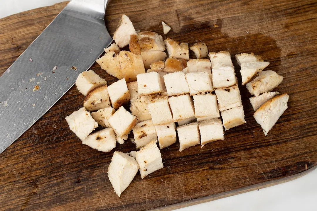 chicken breast cut into chunks on a plate by a knife