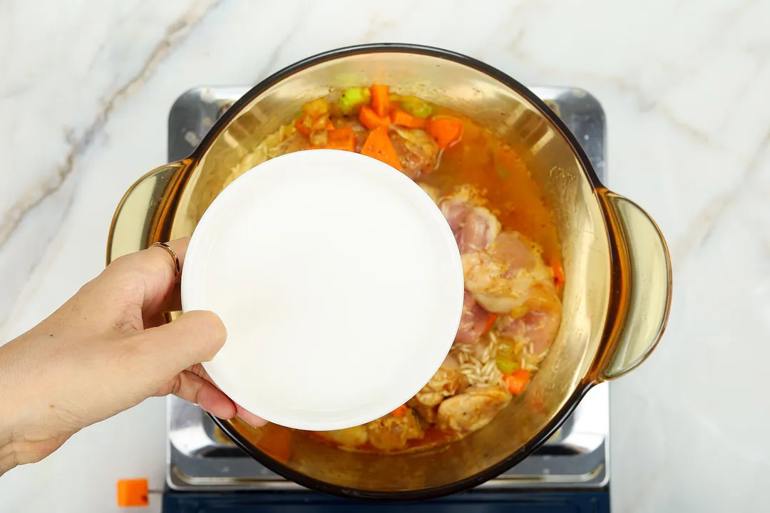 hand holds a bowl of milk on top of a pot of soup