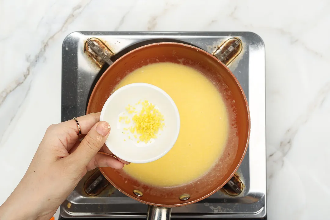 hand holds a small bowl of lemon zest on top of a sauce skillet